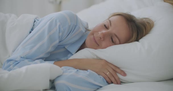 女性が目を覚ますベッドの中で手を伸ばし健康を感じる。女の子はベッドに横になって目を覚ますと甘い伸び. — ストック動画