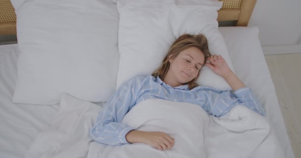 Mulher bonita feliz acordar, sorrindo e esticando os braços em sua cama no quarto. Jovem uso feminino relaxar tempo em casa. Mulher de estilo de vida em casa conceito. — Vídeo de Stock