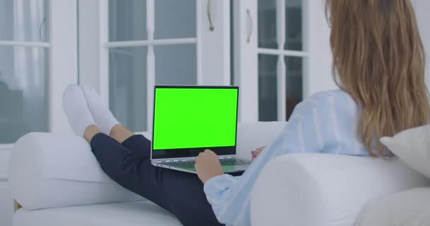 Mladá žena sedí s laptopem na klíně se zelenou obrazovkou během karantény. Chromakey na obrazovce notebooku. Udělejte videokonferenci a promluvte si se zelenou obrazovkou