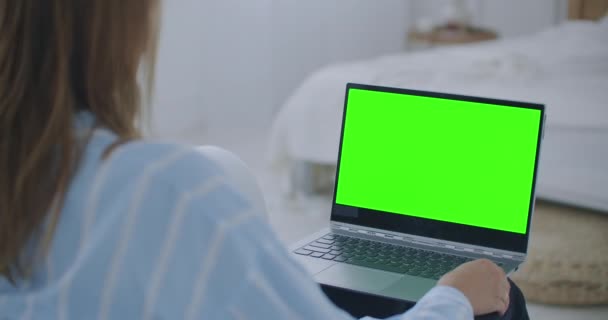Mladá žena doma pracuje na notebooku se zelenou maketou. Sedí na gauči v jeho útulném obýváku. Přes rameno Kamera Shot