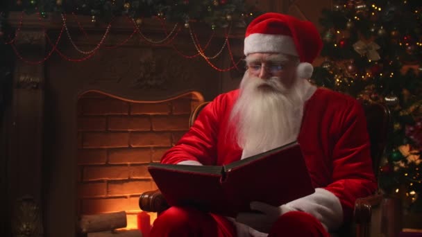 Dobry stary Święty Mikołaj w swoim domu obok kominka i choinki gotowy na Boże Narodzenie — Wideo stockowe