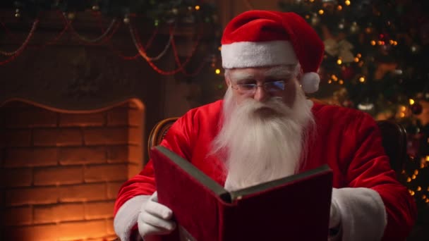 Kerstman zit thuis in een comfortabele stoel en leest een brief — Stockvideo