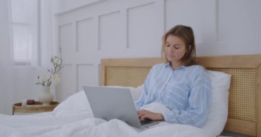 Genç Millennial Kızı Sabah Yatağında Oturuyor, Dizüstü bilgisayar kullanıyor. Beyaz kadın evde şehir içi bilgisayar yatak odasında çalışıyor.