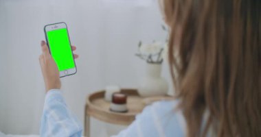 Akıllı telefon kullanan güzel bir kadın, ışık odasında dokunmatik ekran. Genç ve çekici esmer bir kadın sabah yatak odasında arkadaşlarıyla akıllı telefondan görüntülü bir konuşma yapıyor.