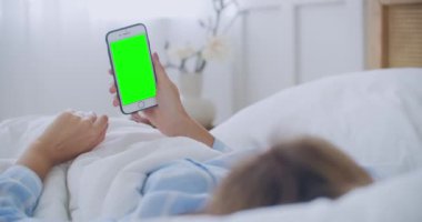Akıllı telefon kullanan güzel bir kadın, ışık odasında dokunmatik ekran. Genç ve çekici esmer bir kadın sabah yatak odasında arkadaşlarıyla akıllı telefondan görüntülü bir konuşma yapıyor.