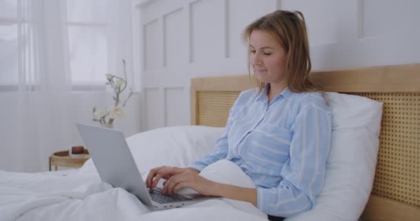 Mulher trabalhando computador portátil na cama. Feliz bonita mulher trabalhando em casa no computador portátil chave do quarto. — Vídeo de Stock