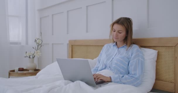 Mulher trabalhando computador portátil na cama. Feliz bonita mulher trabalhando em casa no computador portátil chave do quarto. — Vídeo de Stock