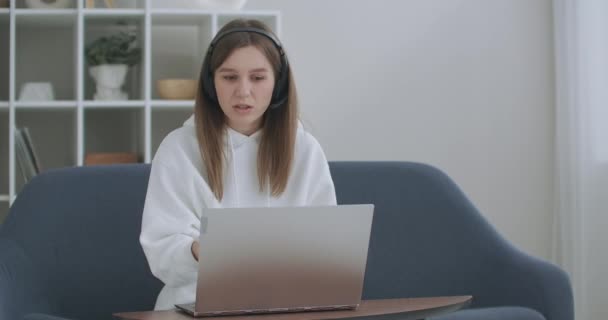 Junge Frau trägt Kopfhörer-Konferenzschaltung auf Laptop Gespräche mit Online-Lehrer studieren, arbeiten von zu Hause aus. Studentin E-Learning mit Computer-Webcam-Chat macht Notizen. Fernstudienkonzept — Stockvideo