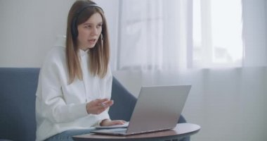 Kadın uzaktan internetle çalışıyor. Mutlu genç iş kadını web kamerasına kulaklık takıyor ve uzaktan video konferans görüşmesi yapıyor. Kadın internet öğretmeni uzaktan sohbet ediyor.