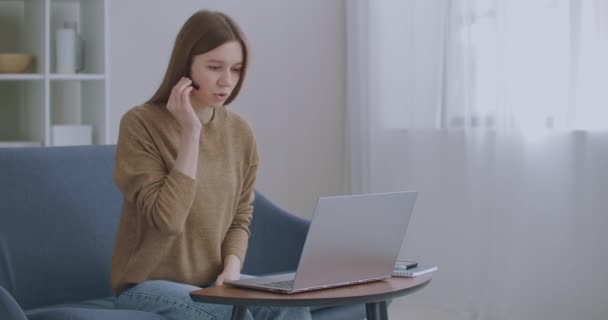 Mujer está consultando en línea, utilizando videollamada y auriculares, hablando y mirando la pantalla de la computadora portátil — Vídeos de Stock