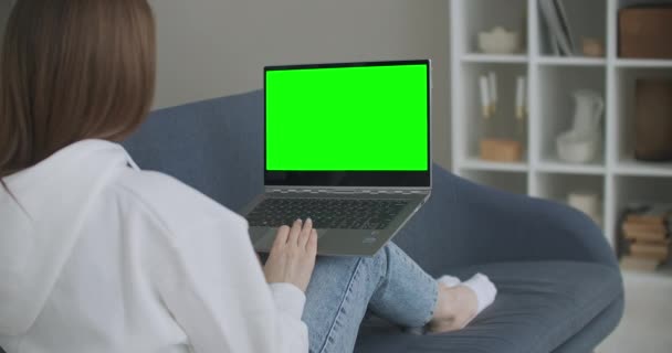 Жінка вдома сидить на дивані працює на портативному комп'ютері з зеленим макетним екраном. Коронавірус Covid-19 карантин дистанційної освіти або робочої концепції. Дівчина за допомогою комп'ютера, перегляд — стокове відео