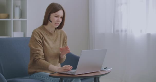 Mujer se está comunicando en línea, utilizando el ordenador portátil con Internet y auriculares con micrófono, chat en línea, soporte técnico — Vídeos de Stock