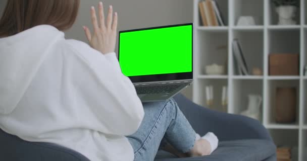 Mulher em casa sentada em um sofá funciona em um computador portátil com tela de falsificação verde. Coronavirus Covid-19 quarentena educação remota ou conceito de trabalho. Menina usando o computador, navegando através — Vídeo de Stock