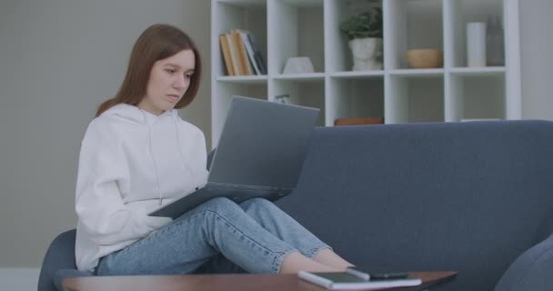 Mujer usando portátil en el sofá en casa. Mujer joven pensativa sentada con el ordenador en el sofá, mirando hacia fuera, concentrarse en el trabajo, sentirse aburrido, necesita motivación adicional, trabajar de forma remota en casa. — Vídeos de Stock