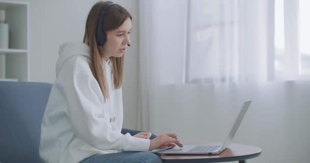 젊은 여성은 집에서 일하는 온라인 교사와 노트북으로 통화를 하는 헤드셋 회의를 합니다. 컴퓨터 웹캠 대화방을 이용하여 학습하는 여학생은 필기를 한다. 거리 교육 개념 — 비디오
