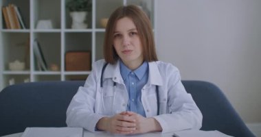 Emekli kadın doktor internette danışmanlık yapıyor, kameraya bakıyor ve kafa sallıyor, kulaklıkla dinliyor, teletıp hizmeti veriyor.