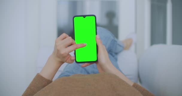 Standpunkt einer Frau in einem modernen Raum, die auf einem Stuhl sitzt und ein Telefon mit grünem Mock-up Screen Chroma Key benutzt, um im Internet zu surfen und Content Videos anzuschauen Blogs, die auf den Bildschirm in der Mitte tippen — Stockvideo