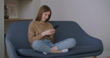 İş kadını ev telefonunda mesaj yazıyor. Genç kız telefonda ağır çekimde sohbet ediyor. Kanepede akıllı telefon kullanarak genç kadın ellerini kapat..