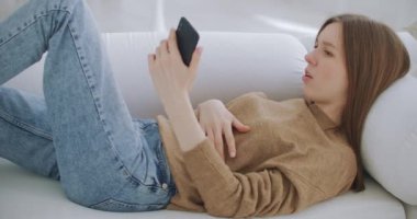 Cep telefonuyla görüntülü arama yapan bir kadın. Oturma odasında modern bir şekilde otururken akıllı telefondan konuşan olgun bir kadın. Teknoloji ve rahatlama kavramı.