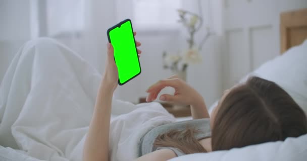 Ung kvinna liggande i sängen gör ett videosamtal till läkaren tittar på den gröna skärmen i chromakey — Stockvideo