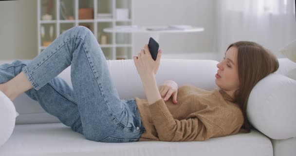 Una donna in videochiamata con un cellulare. Donna matura con parlare su smartphone mentre seduto in soggiorno con interni moderni. Concetto di tecnologia e relax. — Video Stock