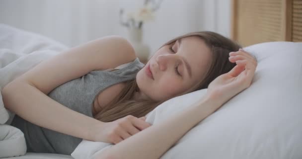 Kranke Frau schläft im Bett unter Decke. Frau bedeckt ihre Ohren mit einer Bettdecke. Junge Frau versteckt sich unter Decke auf einem Bett. — Stockvideo