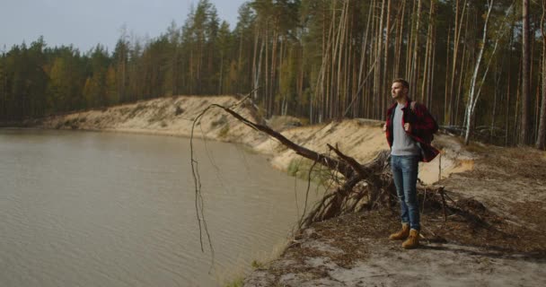 Vandrare med ryggsäck vid solnedgången på toppen av ett berg njuter av solnedgången med en upphöjd hand i en vinnare poserar mot bakgrunden av floden. Resor och semester koncept. — Stockvideo