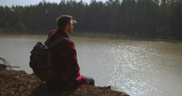 Man With Backpack Comes Sits на The Lake Bank Man Silhouette Wild Duck Swan плаває на озері Озеро Перерослі Зелені очеретяні сонячні відблиски — стокове відео