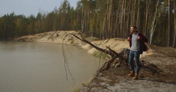 En man går längs en stig i en park nära en sjö tidigt på morgonen på hösten. Man Hill Top. Unge man står på piren med utsträckta armar — Stockvideo