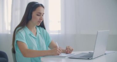 Öğrenci kadın evde oturuyor kulaklık takıyor uzaktan video uygulaması ve dizüstü bilgisayar aygıtı ile konuşuyor e-öğrenme dili öğretmenle ya da sınıf arkadaşıyla birlikte çalışıyor ortak bir görev yapıyorlar, modern teknoloji kavramı.
