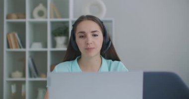 Mutlu genç iş kadını web kamerasına kulaklık takıyor ve uzaktan video konferans görüşmesi yapıyor. Bayan internet öğretmeni evden uzakta sohbet ediyor. Telework konsepti. Web kamerası görünümü