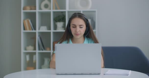 Öğrenci kadın evde oturuyor kulaklık takıyor uzaktan video uygulaması ve dizüstü bilgisayar aygıtı ile konuşuyor e-öğrenme dili öğretmenle ya da sınıf arkadaşıyla birlikte çalışıyor ortak bir görev yapıyorlar, modern teknoloji kavramı. — Stok video