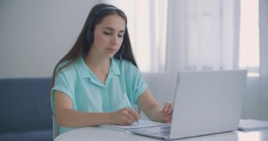 Öğrenci kadın evde oturuyor kulaklık takıyor uzaktan video uygulaması ve dizüstü bilgisayar aygıtı ile konuşuyor e-öğrenme dili öğretmenle ya da sınıf arkadaşıyla birlikte çalışıyor ortak bir görev yapıyorlar, modern teknoloji kavramı.