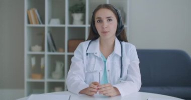 Profesyonel kadın doktor kameraya bakıp konferans görüntüsü alıyor. Web kamerasına konuşan hekim internetten hastayla sohbet ederek uzaktan tıbbi yardım kavramı sağlıyor