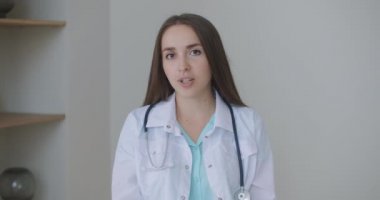 Gülümseyen genç bayan doktor beyaz üniformalı steteskop takıyor video görüntülü görüşme kamerasına bakarak uzaktan görüntülü konuşma, teletıp ve e-sağlık konsepti, webcam
