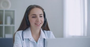 Hastanede dizüstü bilgisayarla video görüşmesi yapan çalışkan Hintli kadın doktor. Gülümseyen genç bayan doktor beyaz üniformalı steteskop takıyor. Video aracılığıyla hastalara danışmanlık yapıyor.
