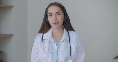 Gülümseyen genç bayan doktor beyaz üniformalı steteskop takıyor video görüntülü görüşme kamerasına bakarak uzaktan görüntülü konuşma, teletıp ve e-sağlık konsepti, webcam