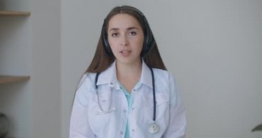 Profesyonel kadın doktor kameraya bakıp konferans görüntüsü alıyor. Web kamerasına konuşan hekim internetten hastayla sohbet ederek uzaktan tıbbi yardım kavramı sağlıyor
