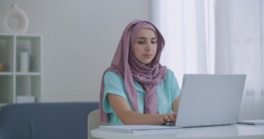 Hristiyan iş arkadaşlarıyla ofiste dizüstü bilgisayarda çalışan Müslüman bir kadın. Dairenin içinde dizüstü bilgisayar kullanan tesettürlü genç Müslüman iş kadını portresi.