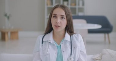 Profesyonel kadın doktor kameraya bakıp konferans görüntüsü alıyor. Web kamerasına konuşan hekim internetten hastayla sohbet ederek uzaktan tıbbi yardım kavramı sağlıyor