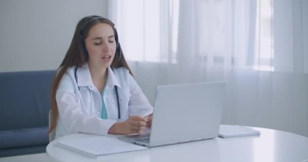 Médico usar fone de ouvido consultar paciente fêmea fazer chamada de vídeo webcam on-line na tela do laptop. Telemedicina videoconferência aplicativo de computador remoto reunião virtual. — Vídeo de Stock