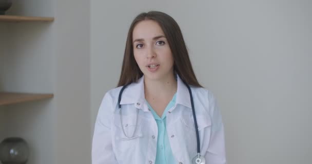 Smiling young female doctor wear white uniform stethoscope consulting online patient via video call looking at camera speaking cam do distance video chat, telemedicine and e-health concept, webcam — Stock Video
