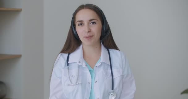 Gülümseyen genç bayan doktor beyaz üniformalı steteskop takıyor video görüntülü görüşme kamerasına bakarak uzaktan görüntülü konuşma, teletıp ve e-sağlık konsepti, webcam — Stok video