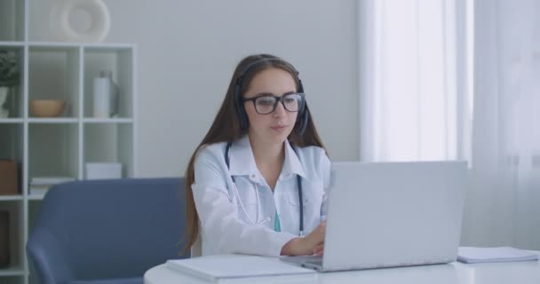 Médica Indiana trabalhadora fazendo videochamada no laptop no hospital. Sorrindo jovem médico do sexo feminino desgaste branco uniforme estetoscópio consulta paciente on-line via chamada de vídeo — Vídeo de Stock