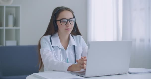 Médica Indiana trabalhadora fazendo videochamada no laptop no hospital. Sorrindo jovem médico do sexo feminino desgaste branco uniforme estetoscópio consulta paciente on-line via chamada de vídeo — Vídeo de Stock