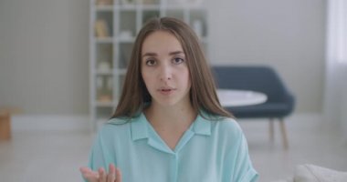 Baş fotoğrafçı kadın kanepeye otur ve kameraya bak. Arkadaşını selamla. Kısa kıvırcık saçlı genç bir kadın video konferans konseptiyle keyifli sohbetler ediyor.