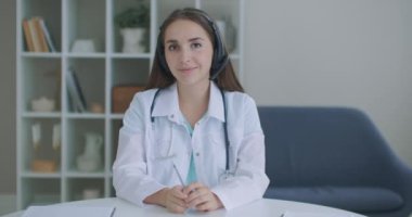 Gülümseyen genç bayan doktor beyaz üniformalı steteskop takıyor video görüntülü görüşme kamerasına bakarak uzaktan görüntülü konuşma, teletıp ve e-sağlık konsepti, webcam