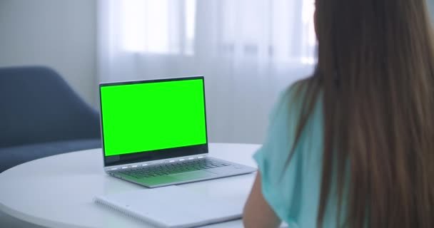 लैपटॉप कंप्यूटर ग्रीन मॉकअप स्क्रीन से नोटपैड में नोट्स ले रही लड़की। लड़की कंप्यूटर पर ऑनलाइन सीख रही है — स्टॉक वीडियो