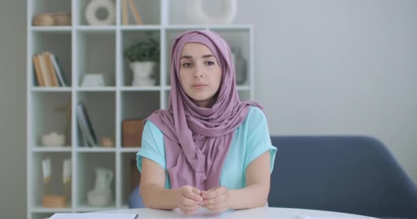 Een vrouw in een hijab kijkt in de camera en knikt stilletjes met haar hoofd en luistert. Gesprek via videolink. Videoconferentie luisteren naar de aanbevelingen van de artsen. — Stockvideo