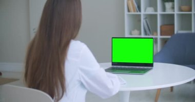 Sağlık çalışanı beyaz önlüklü bir kadın, masadaki ofiste bir tablet kullanıyor, tablet ekranda kromakey, omuzunda bir manzara. Doktor yeşil ekranlı laptopla konuşuyor..